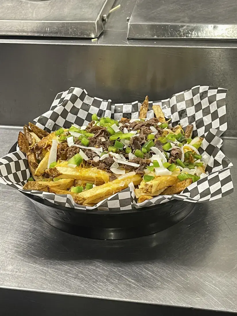 Loaded cheesesteak fries with peppers and onions in a checkered basket, food photography by chef J.O. King