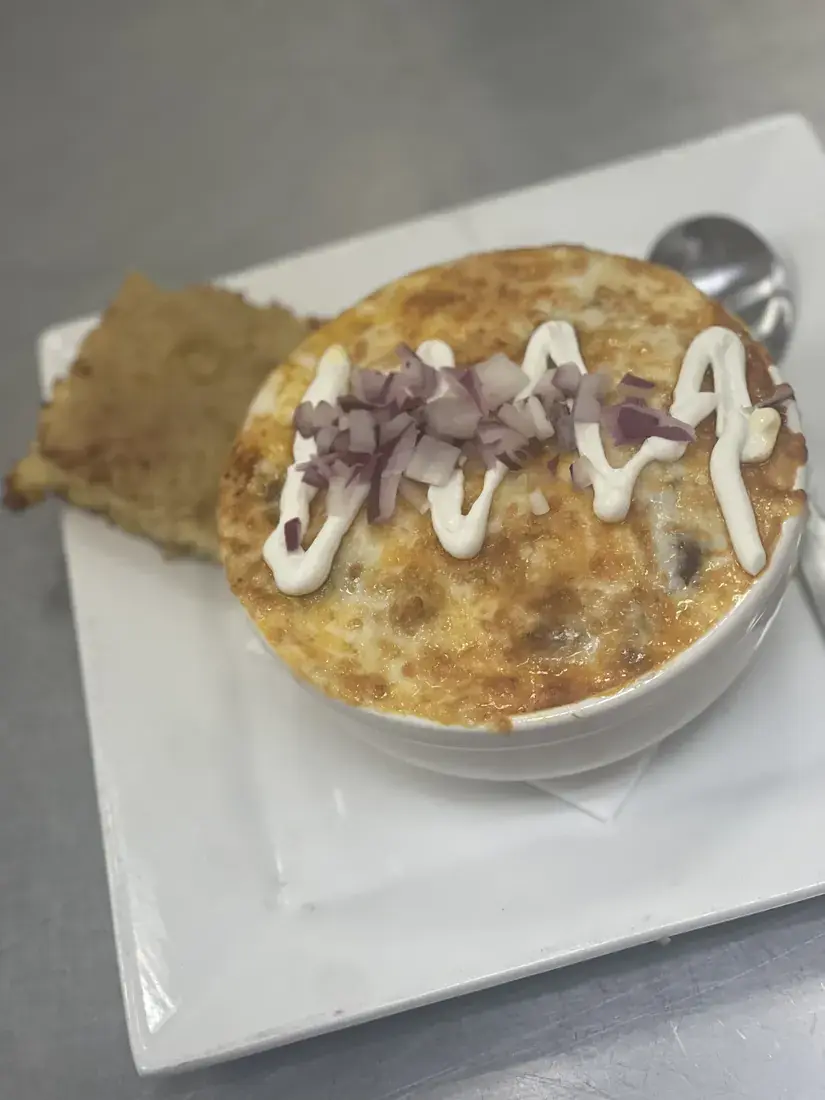 Chili under a broiled cheese crust with red onion and sour cream, served with a flatbread crisp, food photography by chef J.O. King