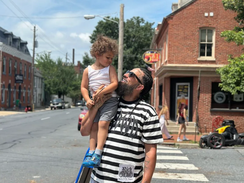 A father holding his child on a sunny city crosswalk — candid lifestyle photography by Pixel Perfect Visuals