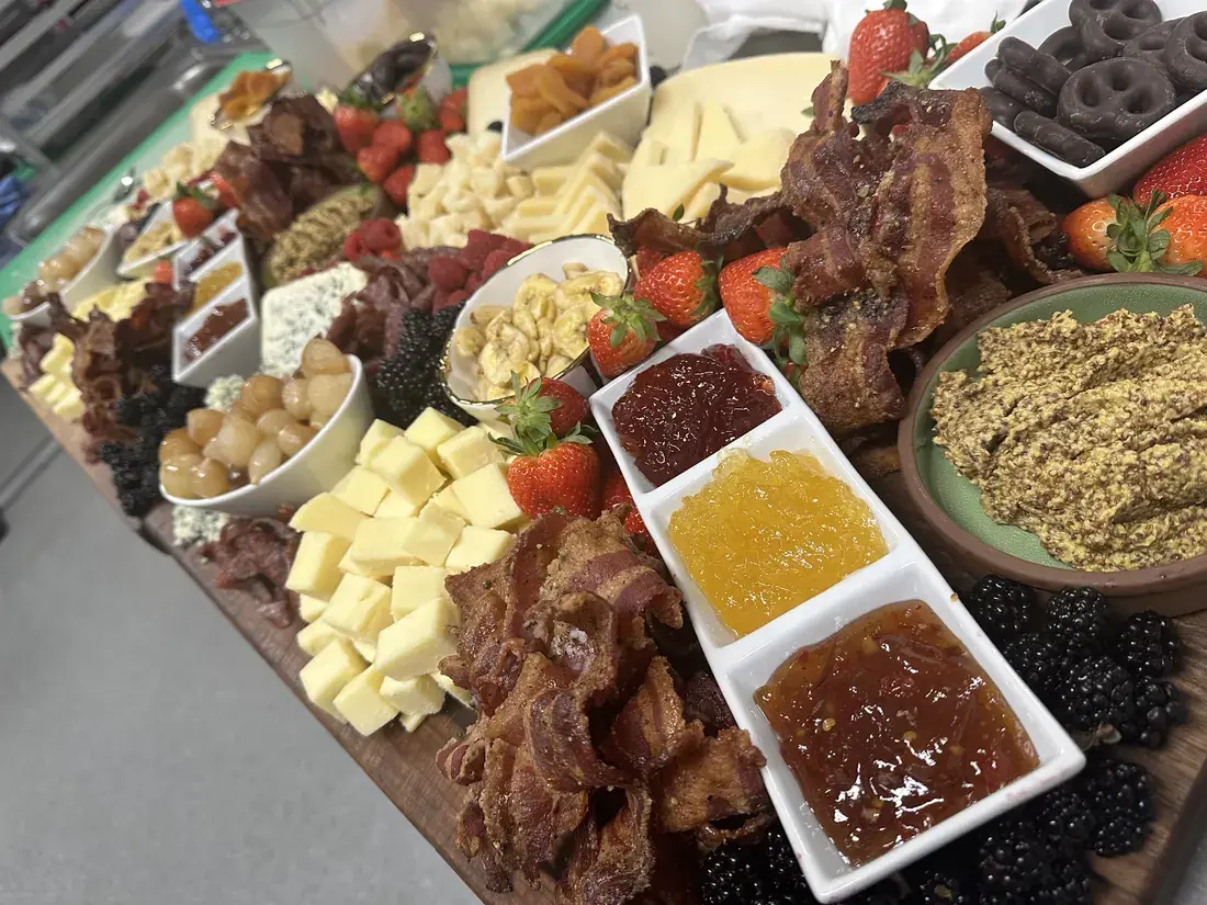 Grazing board loaded with cheeses, candied bacon, berries, jams and chocolate pretzels, food photography by chef J.O. King